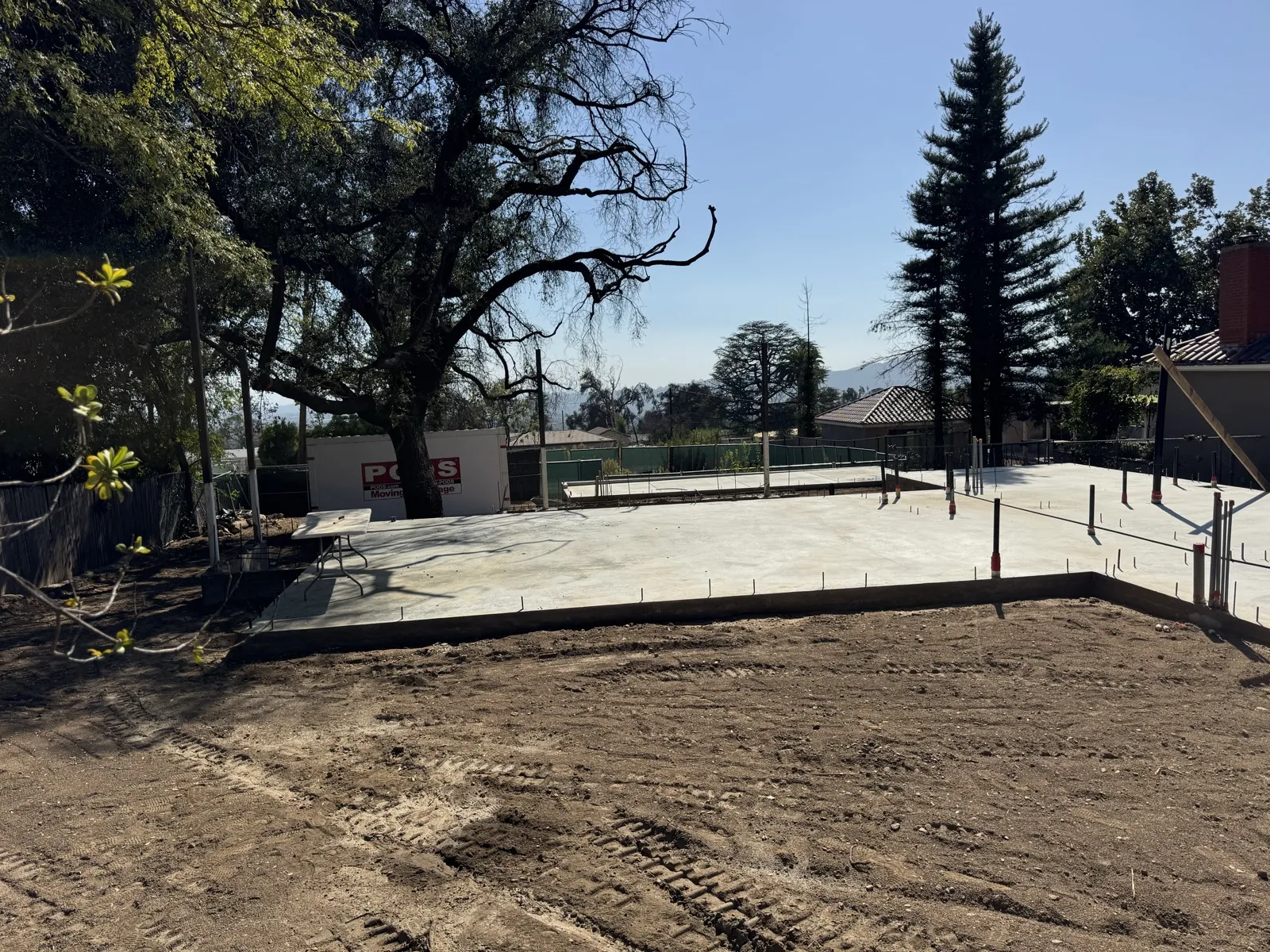 Freshly poured concrete slab foundation at the Las Flores Drive Altadena fire rebuild with rebar stubs and plumbing sleeves below the preserved oak tree