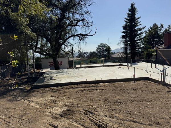 Freshly poured concrete slab foundation at Altadena East Las Flores fire rebuild with rebar stubs and plumbing sleeves below the preserved oak tree