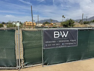 B+W Engineering Grading + Drainage Plans job-site banner on the chain-link fence at the Glenrose Avenue Altadena fire rebuild lot, with rough-graded dirt and the San Gabriel Mountains behind