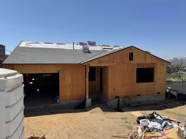 Newly graded bare dirt lot at an Altadena fire-rebuild project in a suburban neighborhood, with bare hills and trees in the background under a clear blue sky