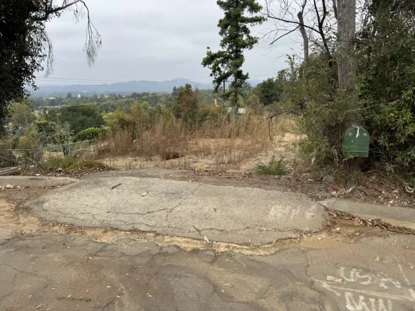 Existing concrete parking pad at the street frontage of the Northaven Lane Altadena fire rebuild lot with green mailbox and downslope view to the valley