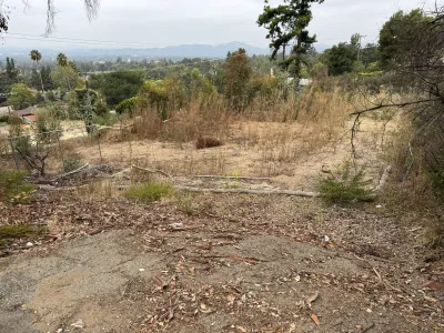 Steep downslope Altadena fire rebuild lot on Northaven Lane looking toward valley with existing dry brush and chain link fence