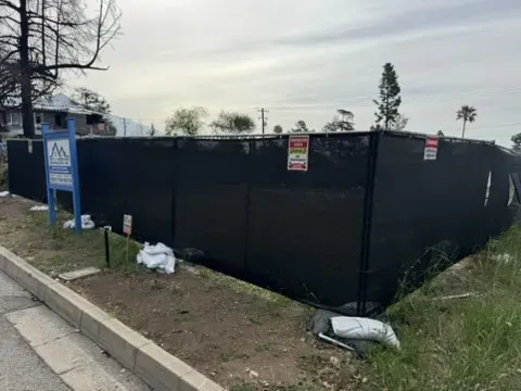 Vacant residential lot in Altadena enclosed by black mesh fencing and sandbags awaiting post-fire rebuild construction