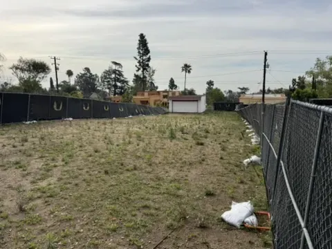 Cleared Altadena lot surrounded by temporary privacy fencing prepared for residential fire rebuild construction