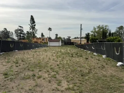 Wide view of vacant Altadena dirt lot with privacy fencing leading to small white garage at rear of property