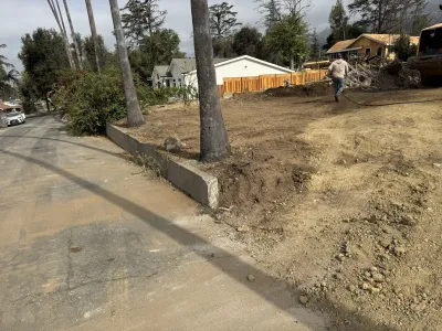 Altadena Punahou Street fire rebuild lot above street level during initial site grading with concrete curb at street frontage and palm trees