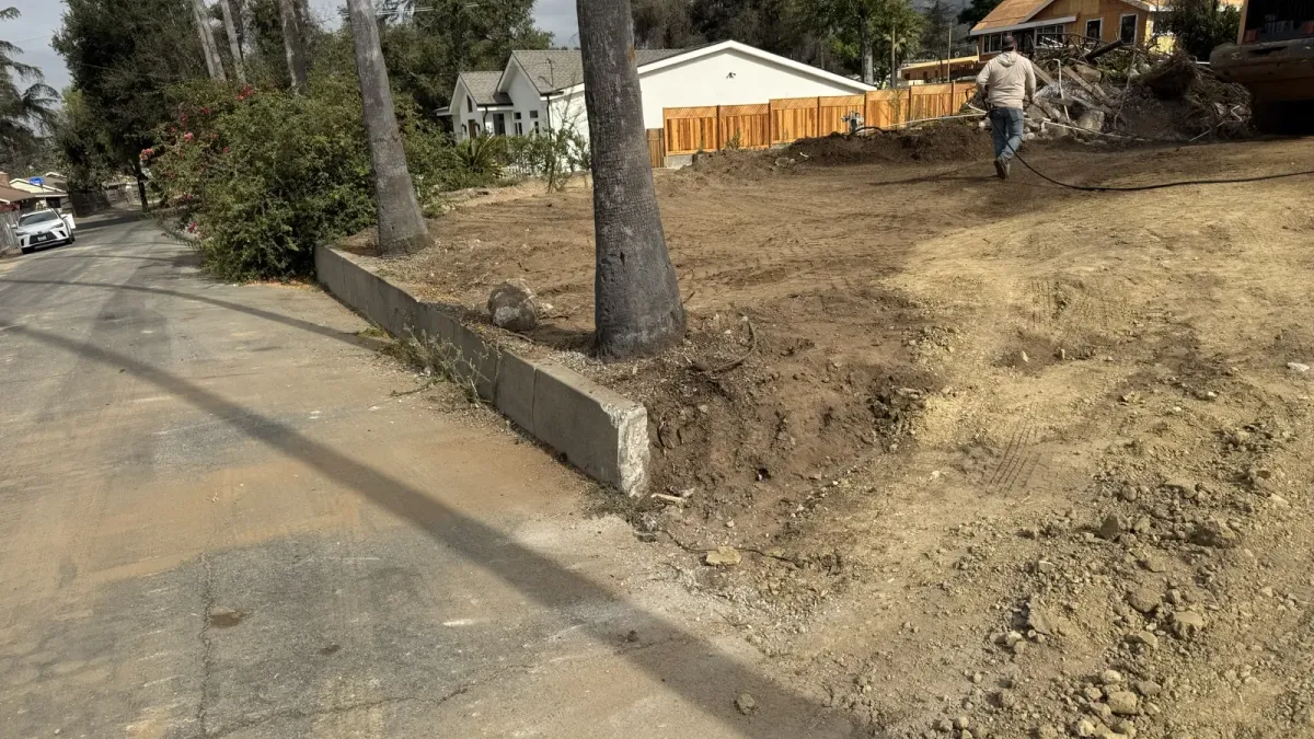 Altadena Punahou Street fire rebuild lot above street level during initial site grading with concrete curb at street frontage and palm trees