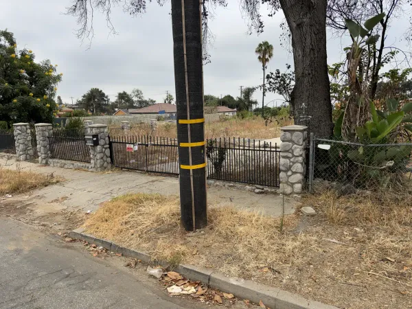 Street frontage of W Mendocino Ave Altadena fire rebuild property showing existing wrought iron gate, stone pillars, and utility pole before construction begins