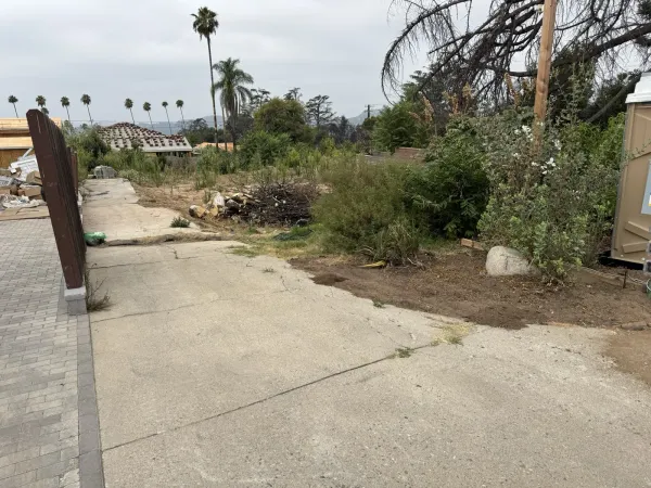 Existing concrete driveway at the Wapello Street Altadena fire rebuild lot looking toward brush pile, palm trees, and neighboring house under construction, used for drainage plan design