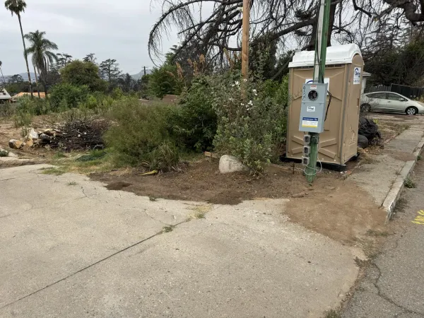 Existing driveway and cleared lot on Wapello Street in Altadena showing United Rentals porta potty, electrical meter, brush pile, and adjacent property access for drainage plan development