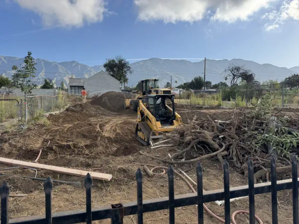 Yellow skid steer loader clearing land with worker doing dust control