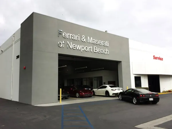 Completed Ferrari and Maserati of Newport Beach luxury dealership in Costa Mesa showing modern gray facade, large structural bay opening, and professional asphalt parking lot with site markings