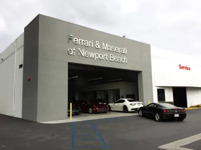 Completed Ferrari and Maserati of Newport Beach luxury dealership in Costa Mesa showing modern gray facade, large structural bay opening, and professional asphalt parking lot with site markings