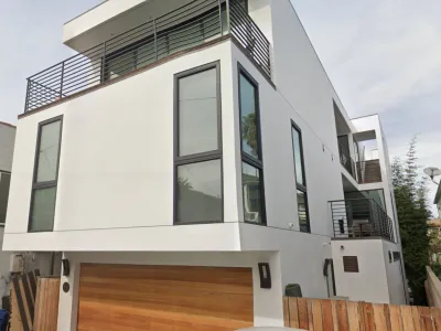 Completed modern three-story white stucco residence on 18th Street Hermosa Beach with cantilevered facade, black-framed windows, wood garage door, and professional landscaping