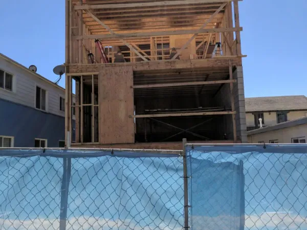 Urban construction site for 18th Street residential project in Hermosa Beach showing wood framing, I-joists, and plywood sheathing with chain-link fence enclosure