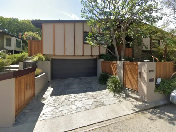 Modern mid-century residence at Devlin Drive above Sunset Strip with vertical wood batten siding, flagstone driveway, cedar gates, and mature landscaping