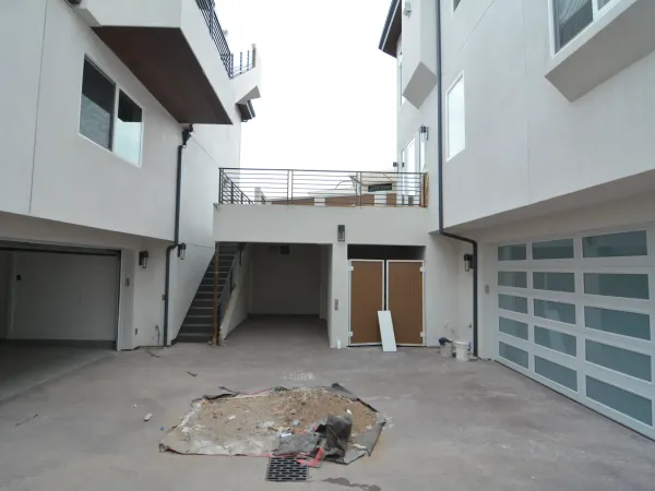 New construction residential driveway and courtyard between two modern white stucco buildings with concrete surface, storm drain, and downspouts for drainage