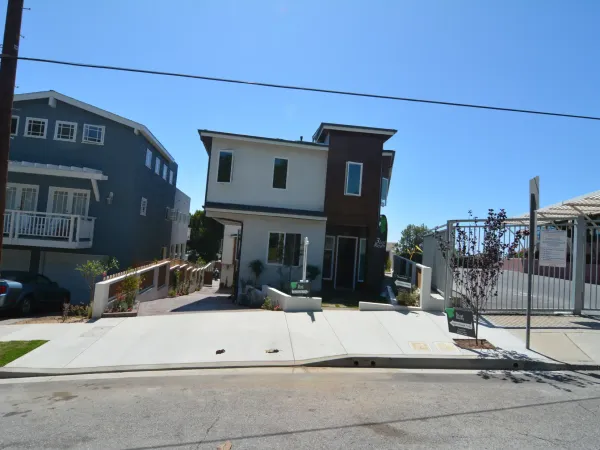 Two modern residential properties on sloped lot showing white stucco and dark wood siding, sloped concrete driveways, and tiered masonry retaining walls
