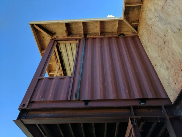 Container steel foundation interface with corrugated metal walls and structural I-beam support at ground level