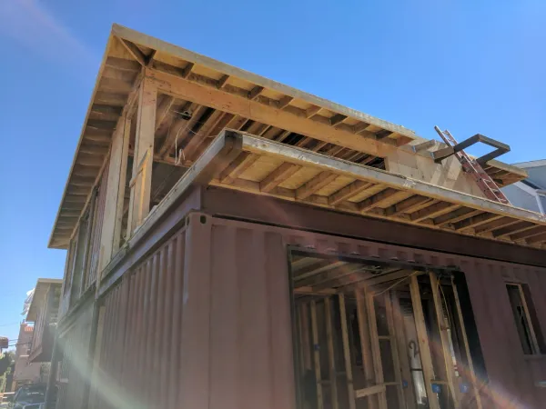 Hybrid construction showing shipping container ground floor integrated with timber framing for second level and roof