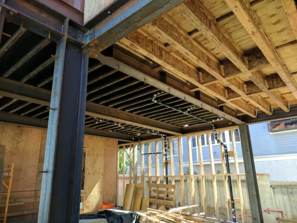 Interior steel I-beam framing integrated with engineered wood floor joists and black vertical drainage pipe system