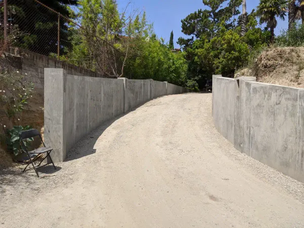 A graded dirt driveway under construction featuring a gentle upward slope and newly installed concrete retaining walls on both sides