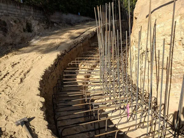 Hillside construction site featuring deep excavation and grading for a curved retaining wall with steel rebar reinforcement