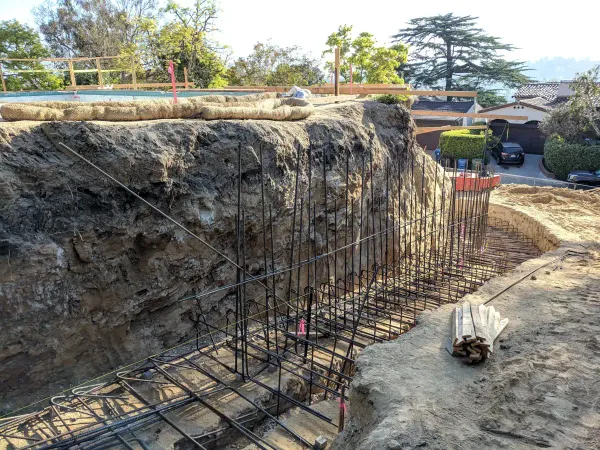 Excavation and site grading for a residential retaining wall with large steel rebar cage against a steep earthen slope