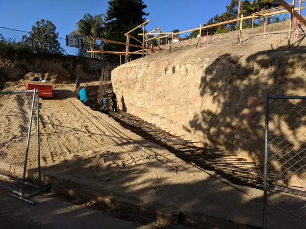 Construction site showing slope grading and foundational work for a retaining wall on a steep hillside with rebar reinforcement installation