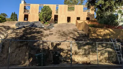 Two-story residential house under construction with OSB sheathing sits atop a steep, newly graded dirt slope with erosion control measures