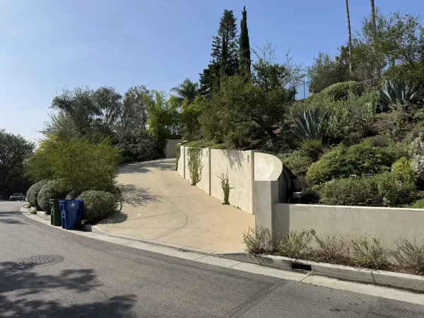 Finished smooth beige concrete retaining wall bordering a curved paved driveway on a Silver Lake hillside, green and blue wheeled bins at the Redcliff Street curb