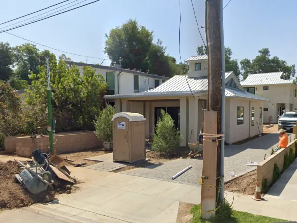 Modern two-unit residential construction with stucco walls and metal roof in South Pasadena. Covered trellis parking structure in center with paver driveway