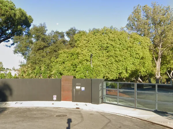 Modern residential entrance at 3523 Wrightwood Court with charcoal grey perimeter wall, Corten steel accent panel, glass driveway gate, and mature oak trees